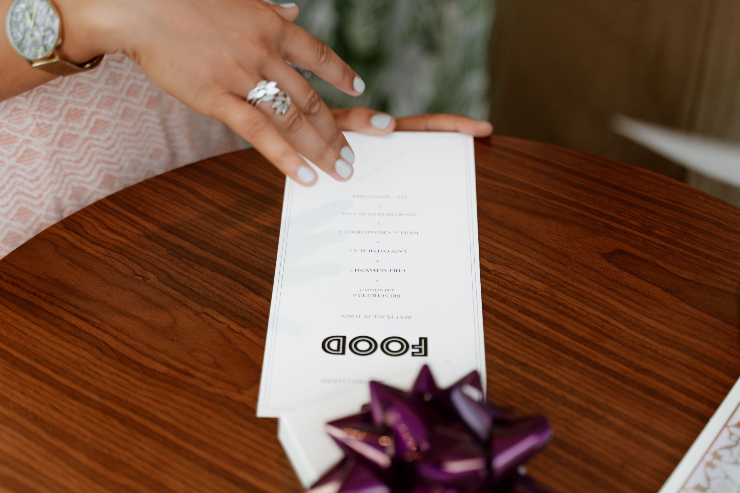 Close-up of a hand holding a restaurant menu at a table, representing the importance of clear dietary and allergen information.